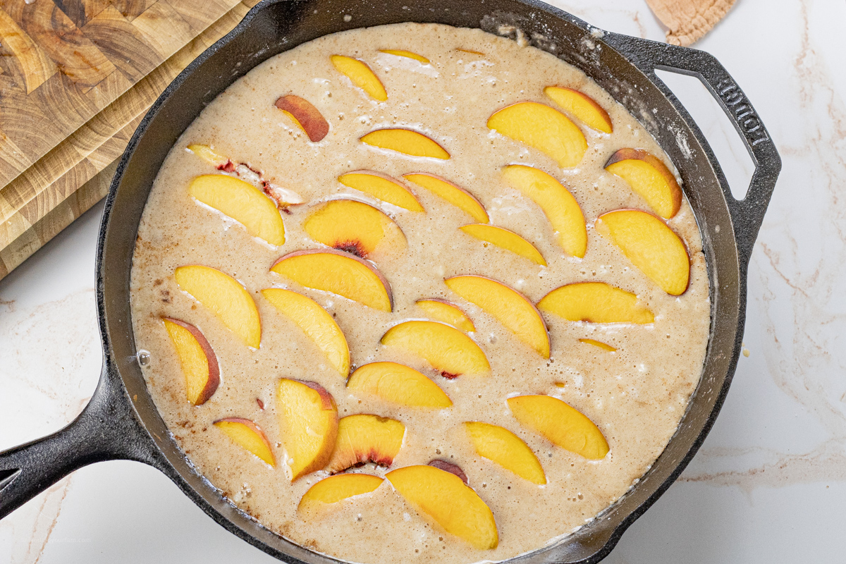peaches layered on top of cobbler batter in a cast iron pan