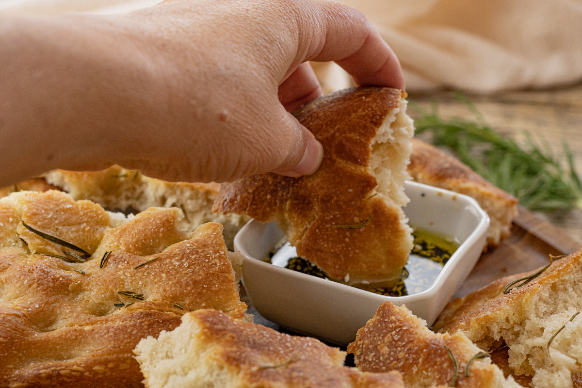 hand dipping piece of bread in olive oil dip
