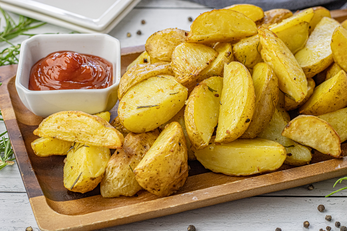 gold potato wedges on a wooden serving platter with a bowl of ketchup