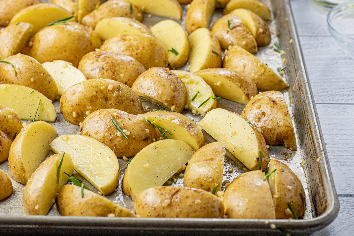 sliced golden potatoes on a baking sheet seasoned with garlic, salt, pepper and rosemary
