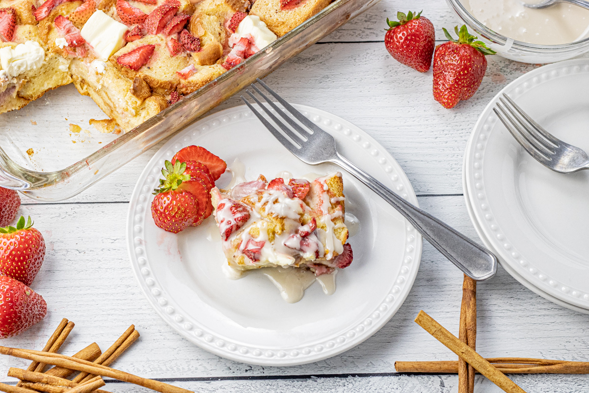 a slice of french toast casserole with strawberries on a white plate and drizzled with vanilla icing