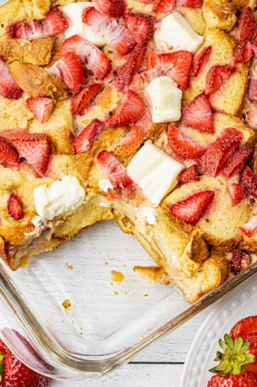 pan of strawberry cream cheese french toast with a piece missing in a glass baking dish