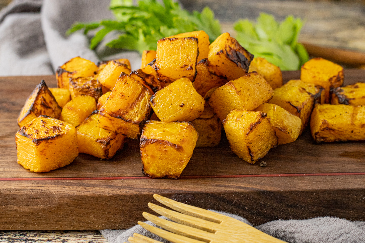 cooked cubes of squash on a wooden cutting board