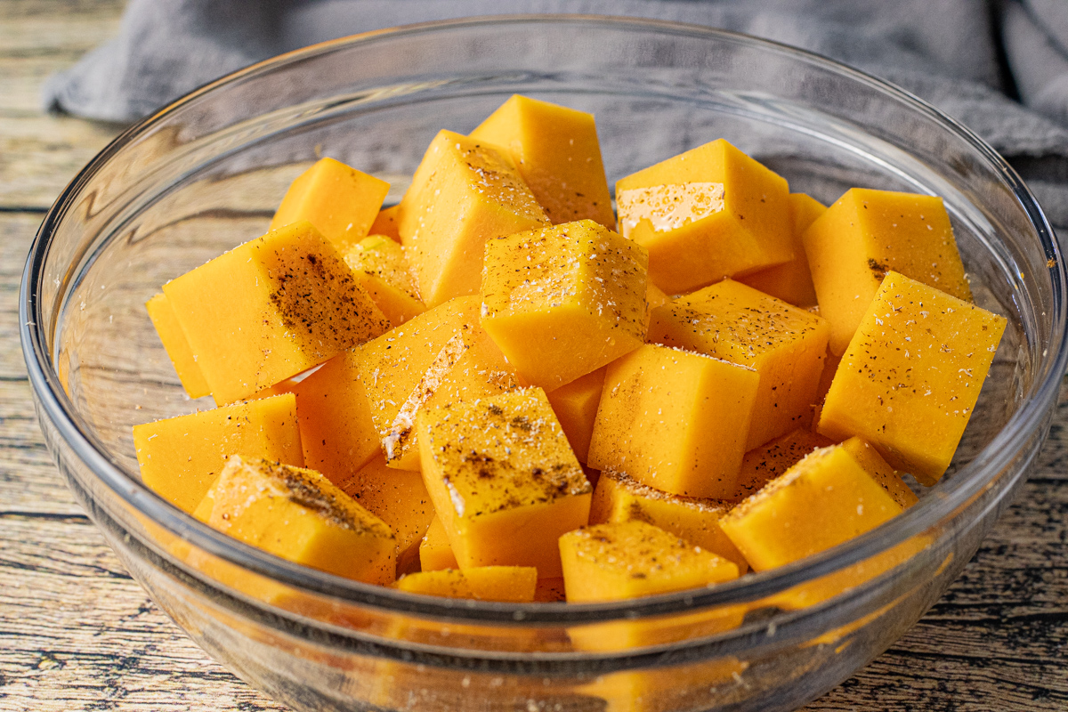 squash cubes in a glass mixing bowl seasoned with salt, pepper, cinnamon and nutmeg