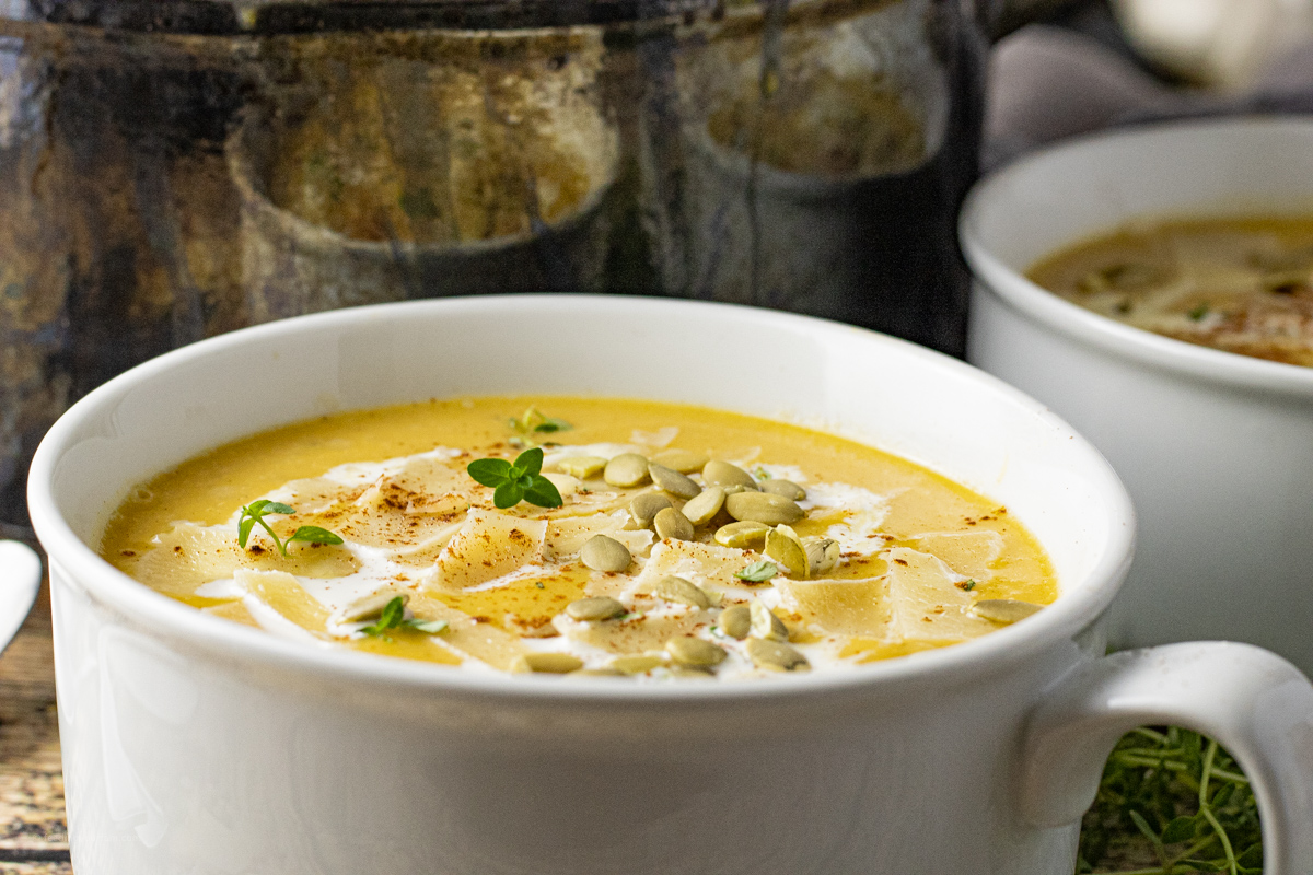 up close picture of butternut squash soup topped with pumpkin seeds, cream and cheese in a white bowl