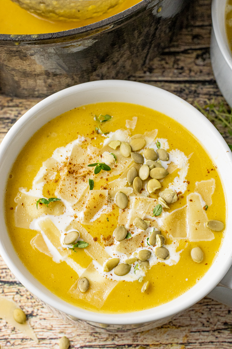 white bowl filled with butternut squash soup topped with pumpkin seed, cream and cheese