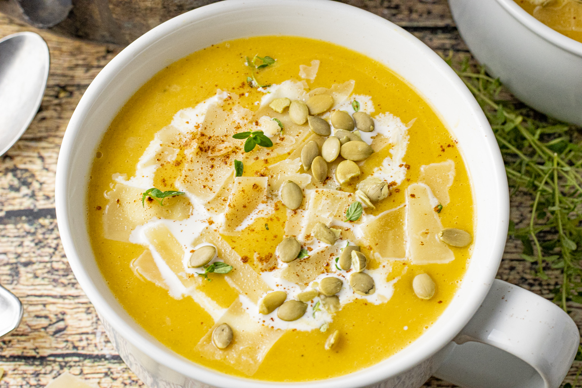 white bowl filled with butternut squash soup topped with pumpkin seeds and cheese