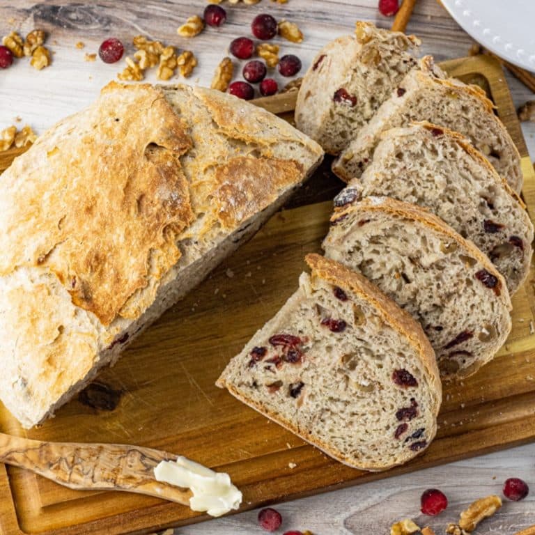 bread made with cranberries and walnuts sliced on a wooden cutting board