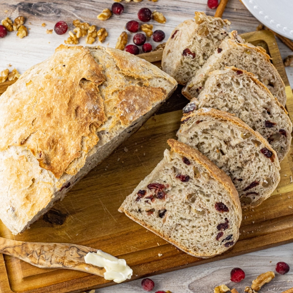 bread made with cranberries and walnuts sliced on a wooden cutting board