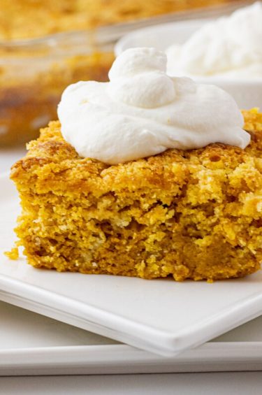 piece of pumpkin cake on a white plate topped with whipped cream