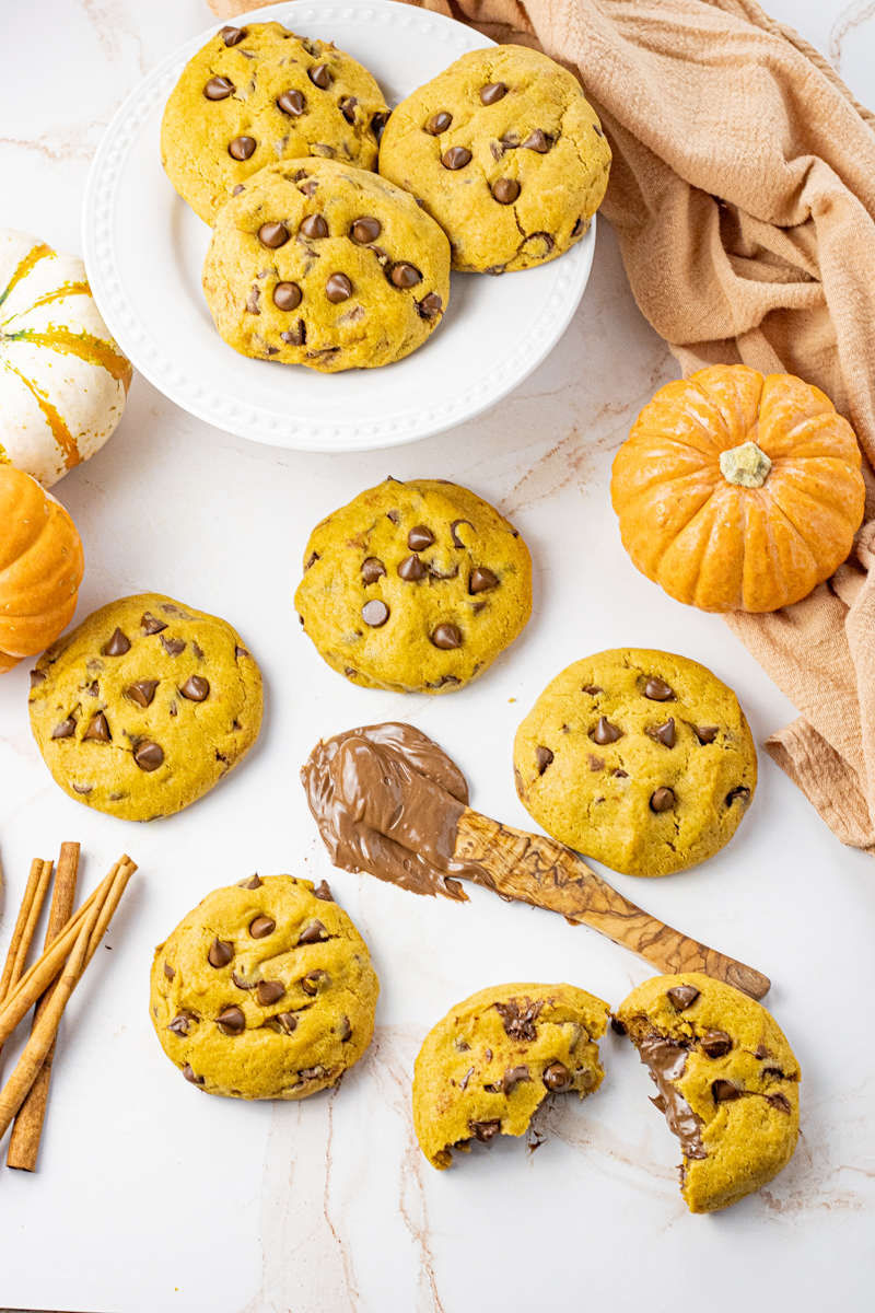 pumpkin cookies with chocolate chips, one broken in half that has been stuffed with chocolate spread