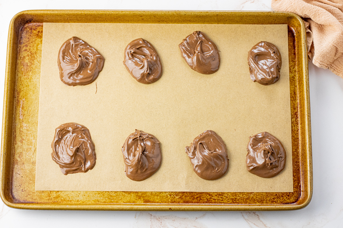 scoops of chocolate spread on a parchment lined baking sheet.