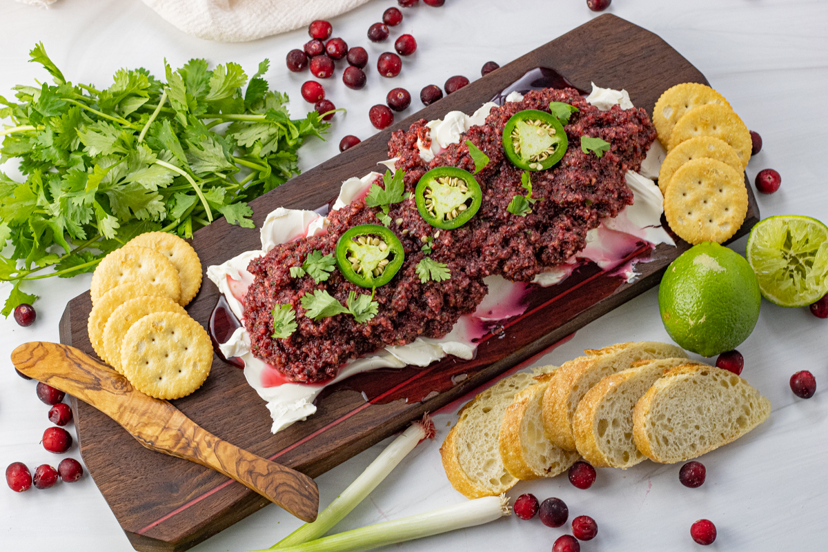 cream cheese spread on a wooden platter topped with cranberry sauce