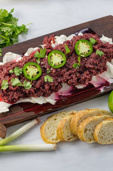 cream cheese topped with salsa made from cranberries on a wooden serving platter