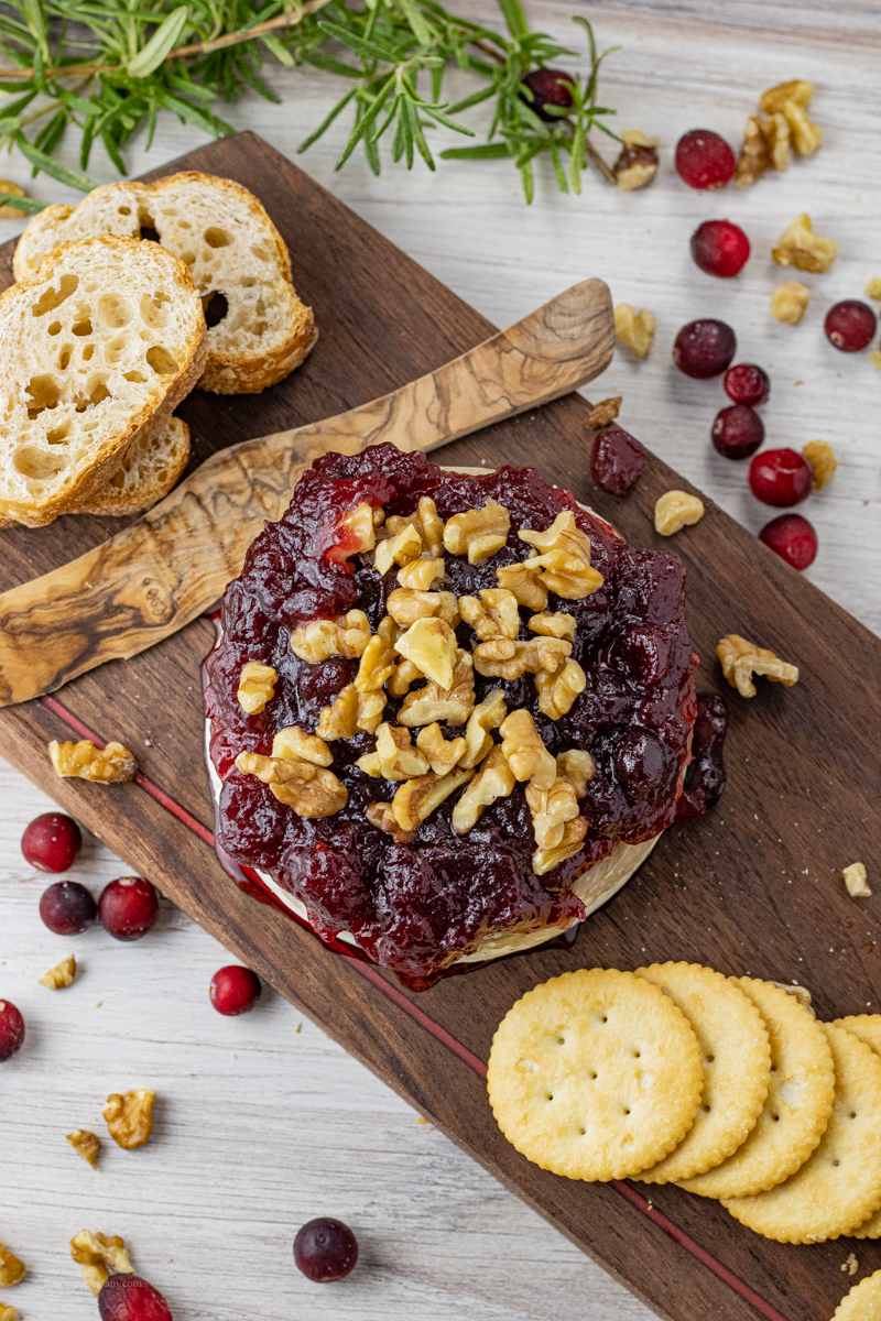 brie cheese wheel topped with cranberries and chopped walnuts