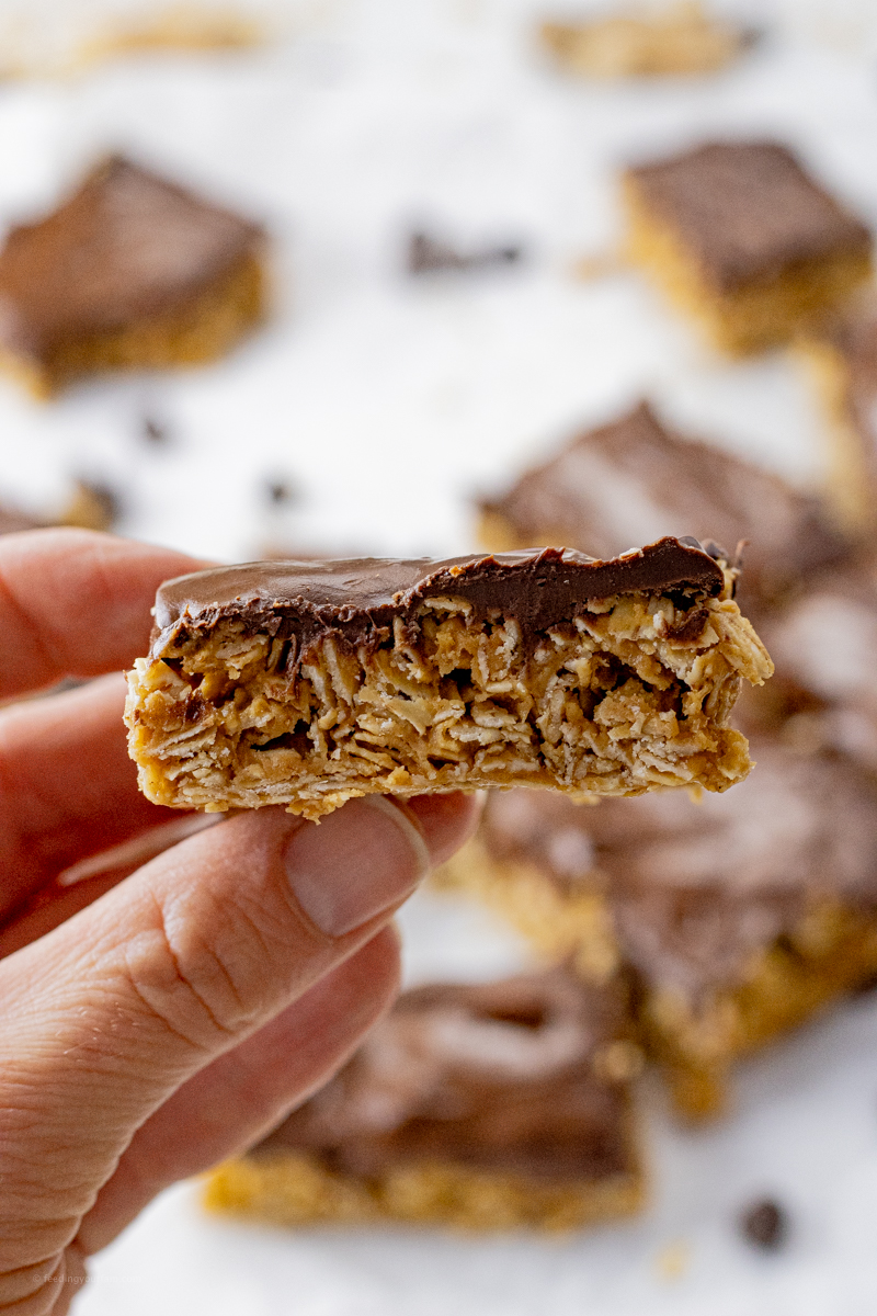 hand holding up a peanut butter oatmeal bar topped with chocolate
