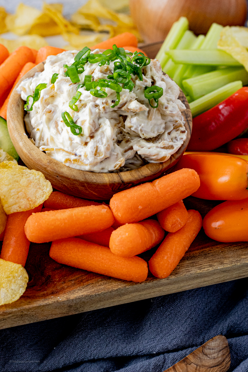 small wooden bowl with creamy onion dip surrounded by veggies and chips