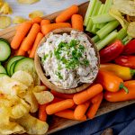 dip with caramelized onion surrounded by chips and vegetables