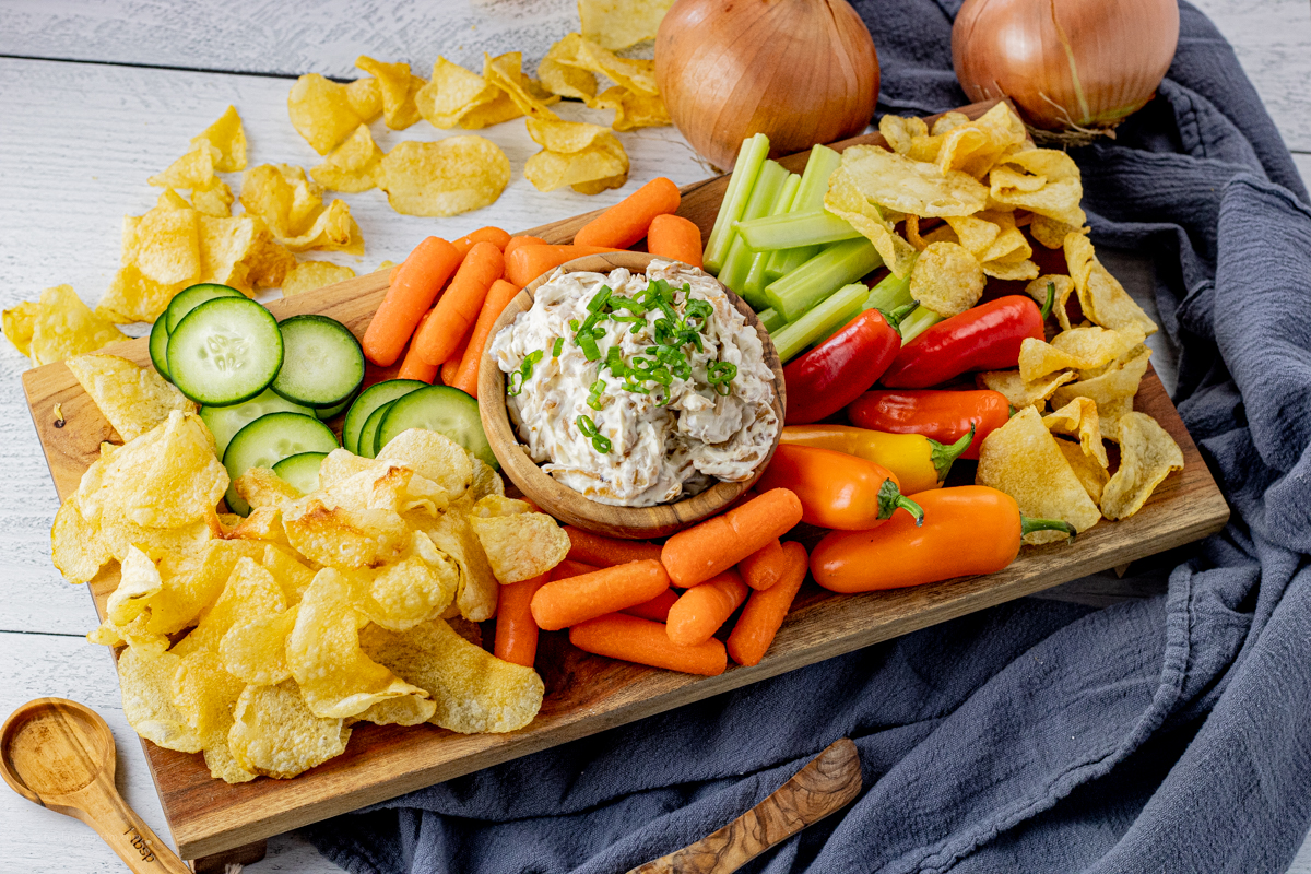 onion dip in a wooden bowl, surrounded by veggies and chips