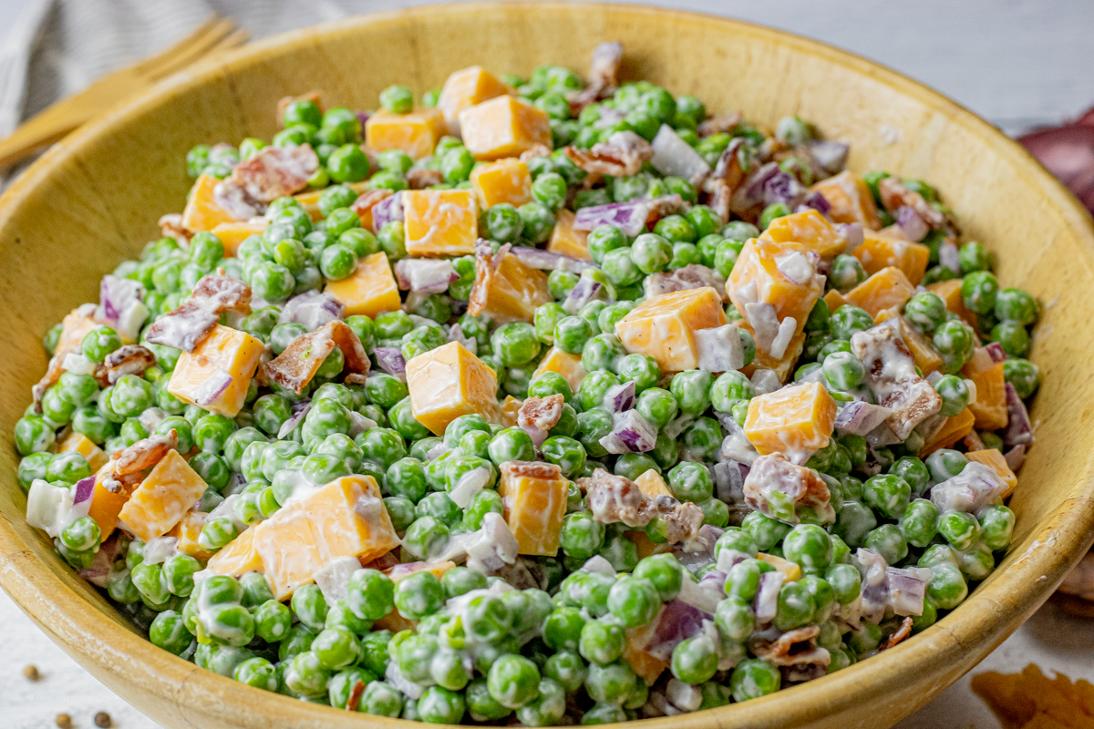 creamy salad with peas, cheese, bacon and red onion in a wooden salad bowl