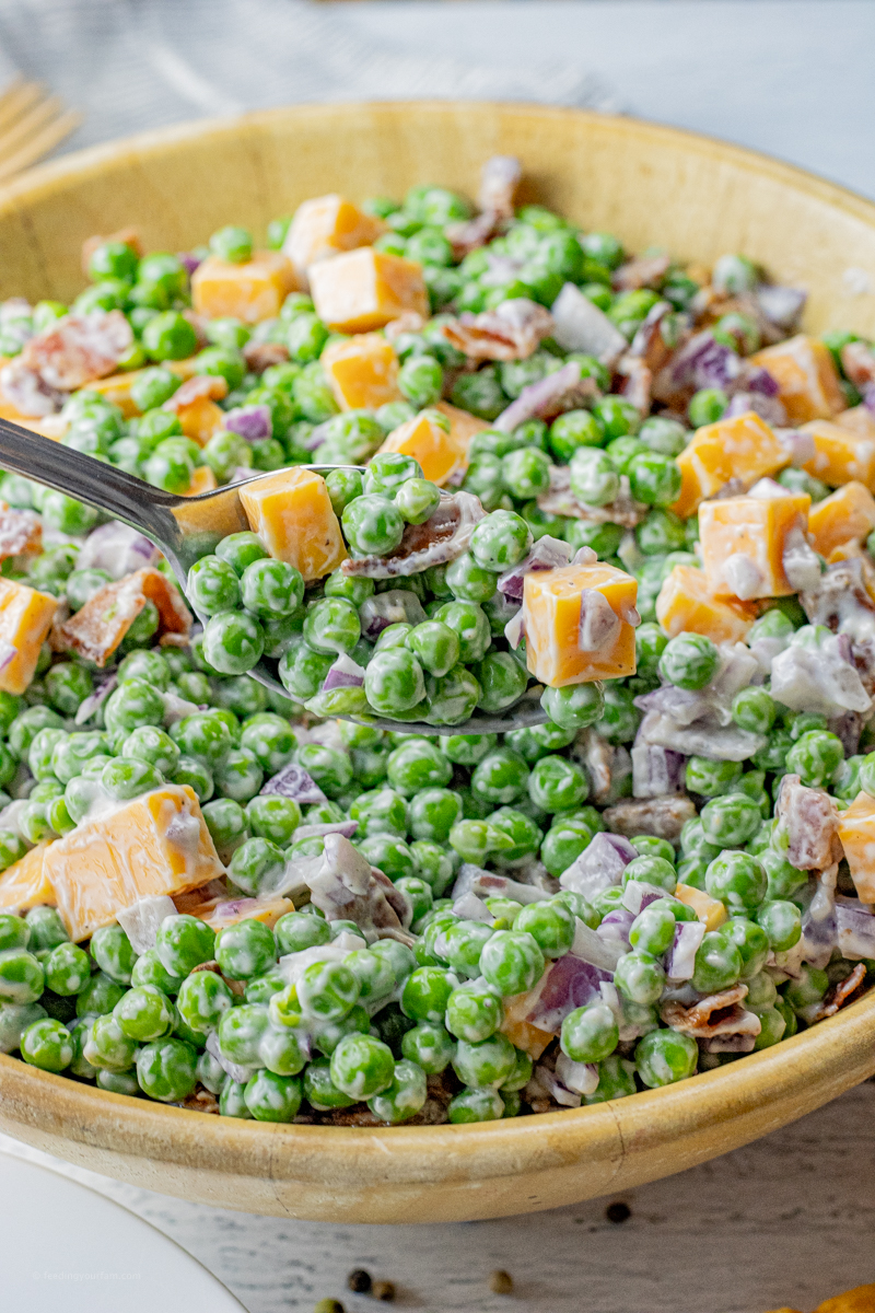 spoon holding up a scoop of salad with green peas, bacon, red onions and cheese