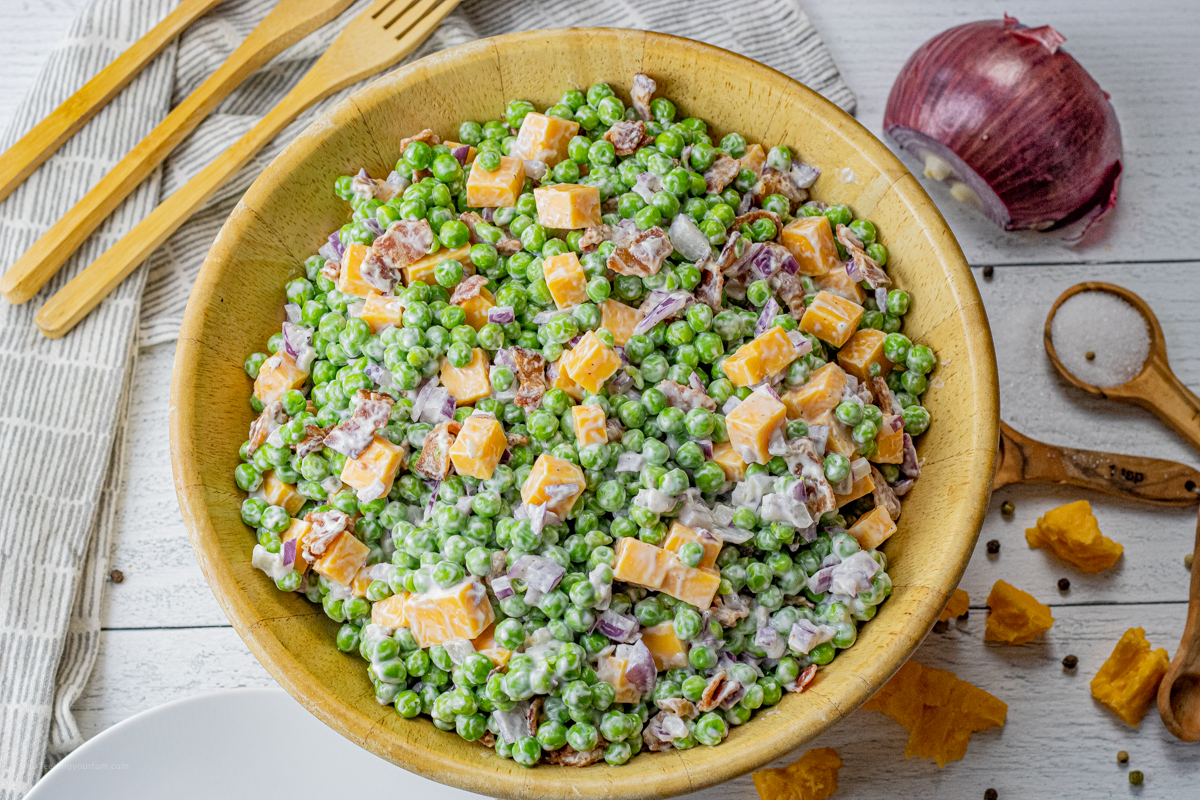 green pea salad with bacon and cheese in a large wooden serving bowl
