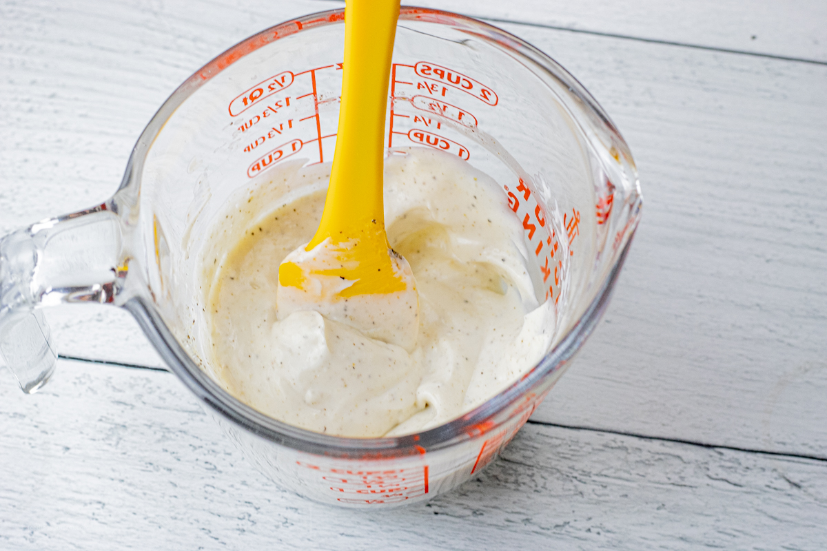 sour cream dressing in a mixing cup with a yellow spatula