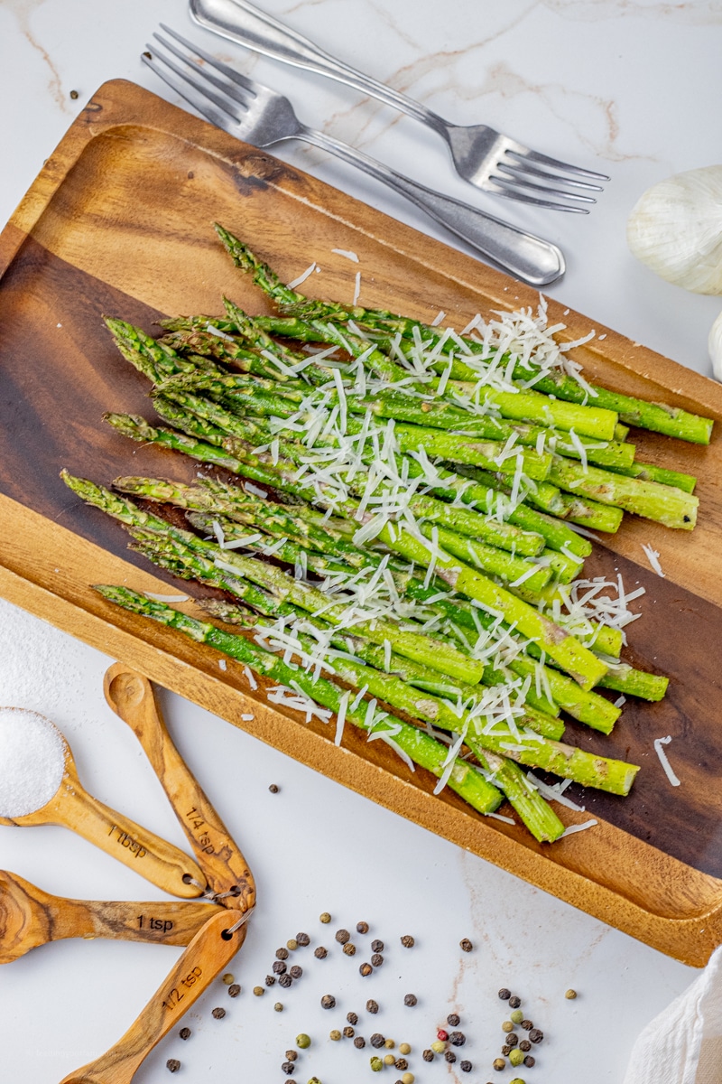 cooked, green asparagus spears on a wooden platter topped with shredded parmesan cheese
