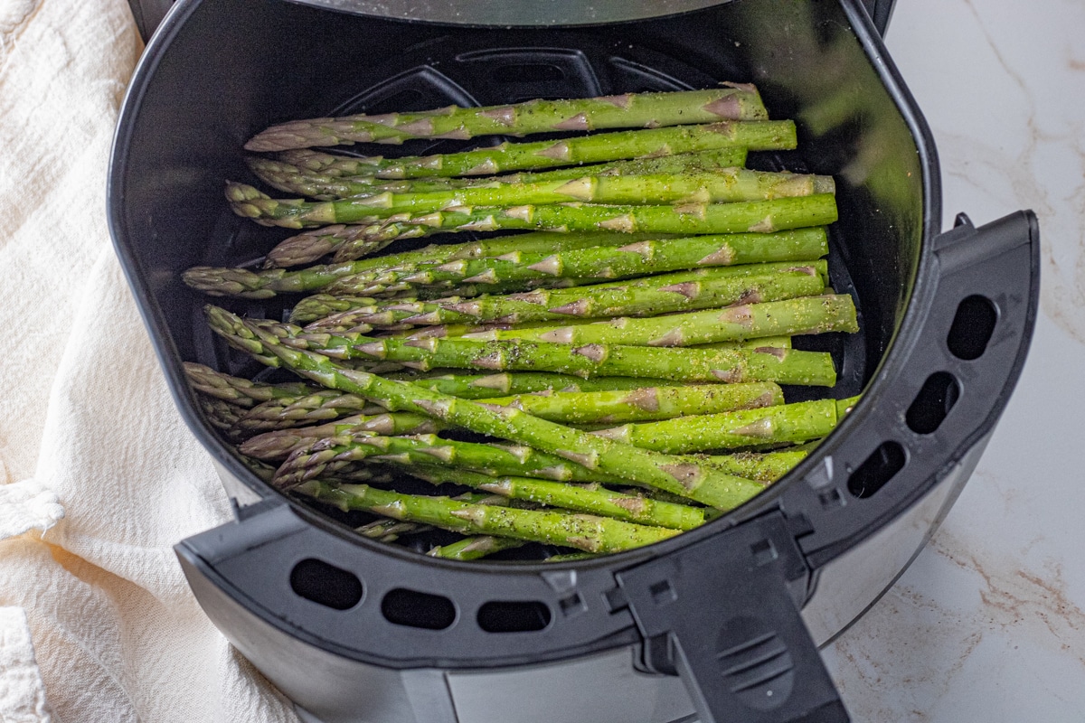 green uncooked asparagus spears in the basket of an air fryer