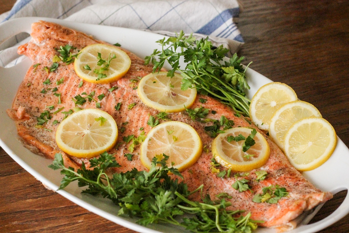 baked salmon topped with lemon slices and parsley on a white serving platter
