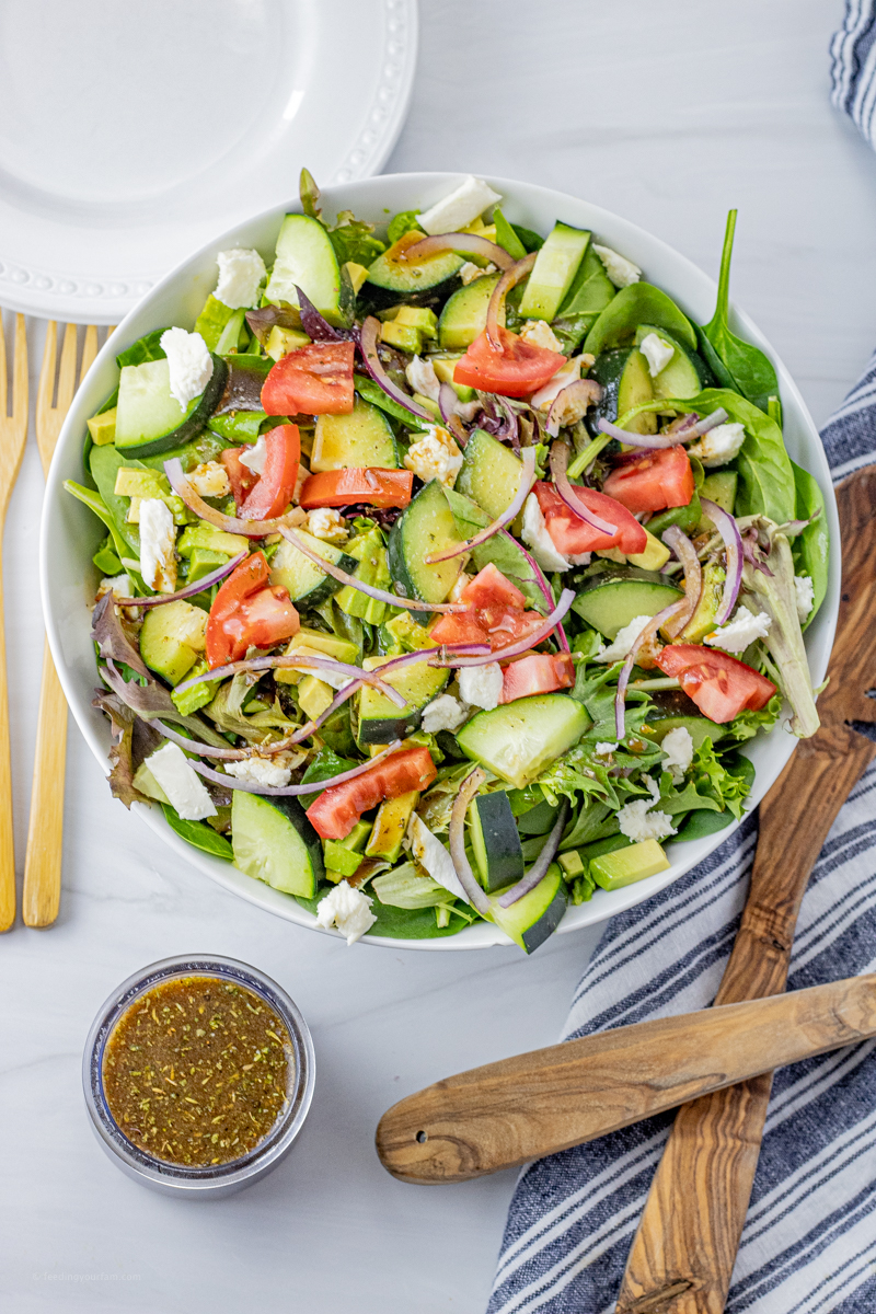 large green salad in a white bowl with a small glass jar of vinaigrette next to it