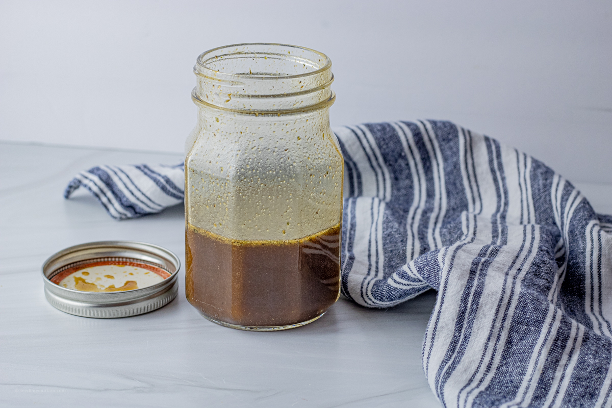 glass jar with balsamic dressing inside and the lid on the table next to the jar