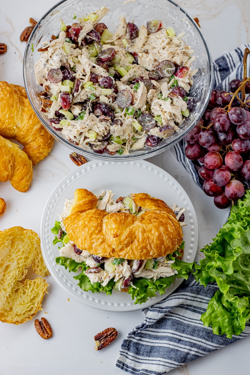 shredded chicken salad with grapes, celery, and green onions in a glass mixing bowl