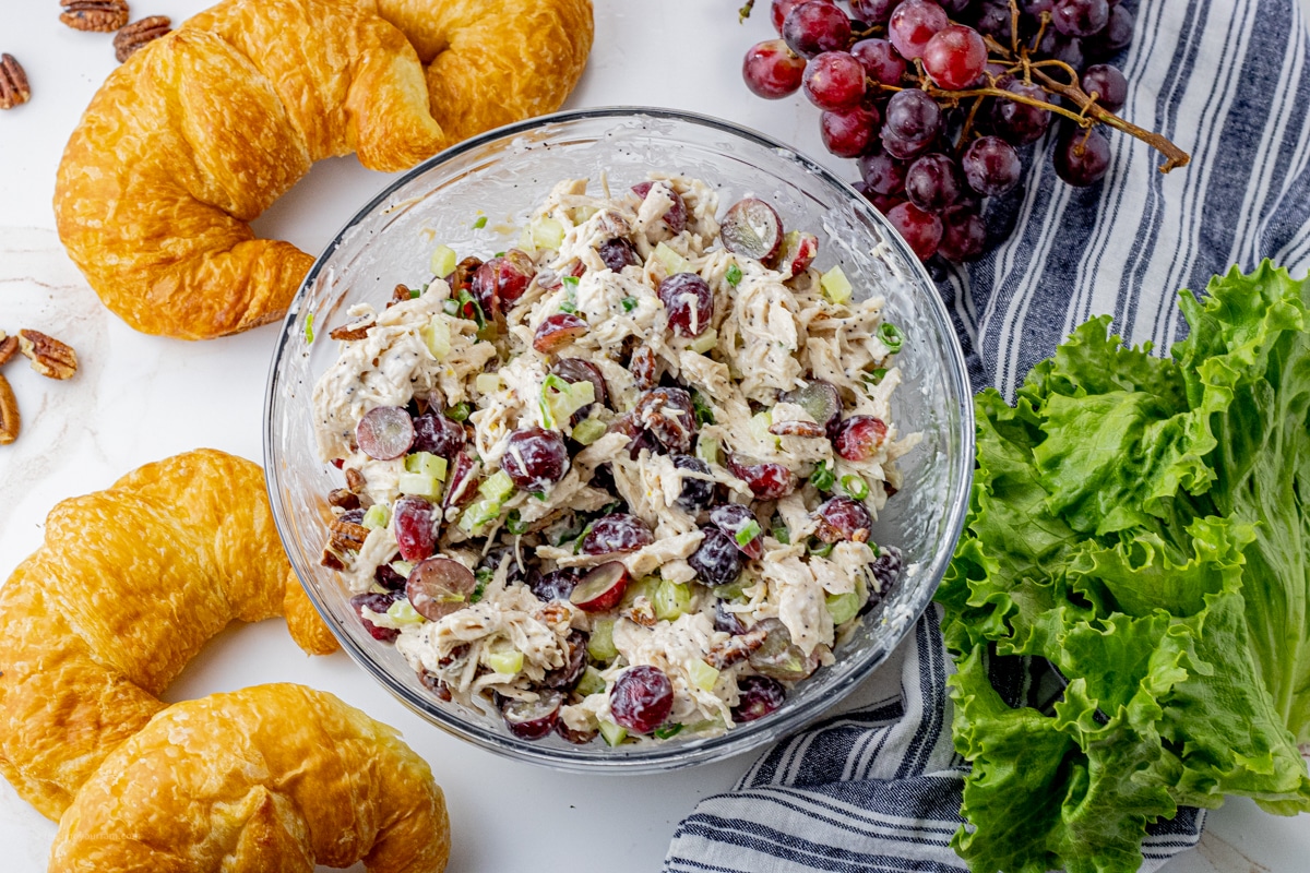 creamy chicken salad with red grapes, celery, green onions and pecans in a glass mixing bowl. 