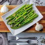 plate of asparagus cooked with garlic and butter on a white plate