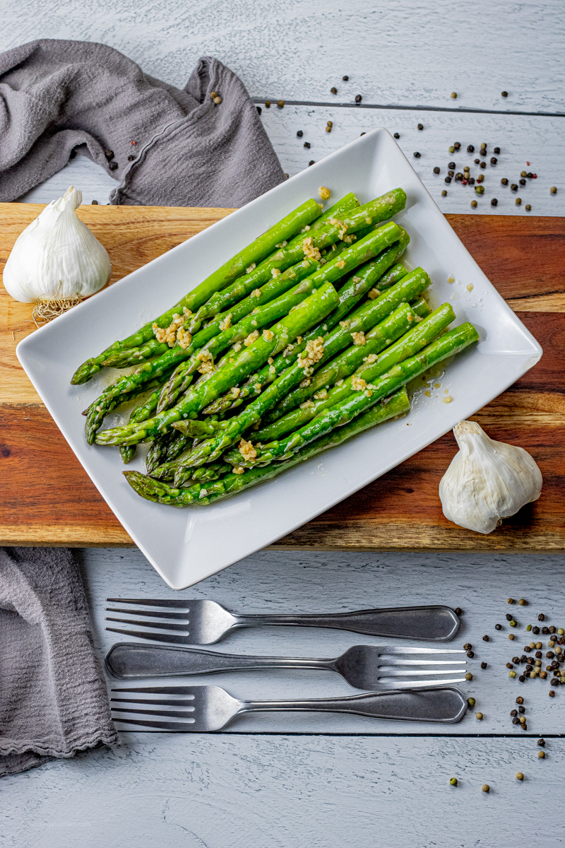green asparagus spears topped with garlic and butter on a white serving platter