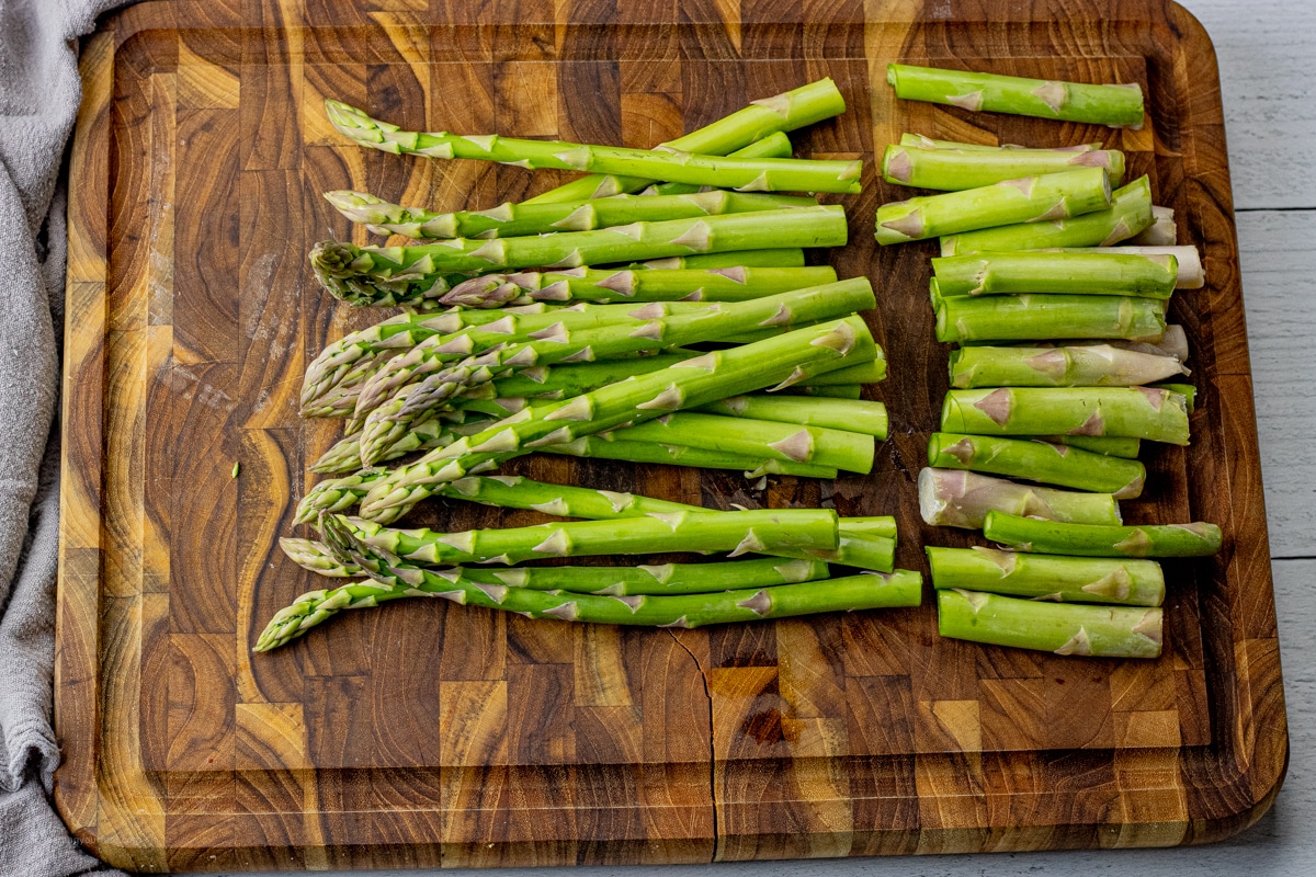 asparagus spears on a wooden cutting board sliced with the woody bottoms removed
