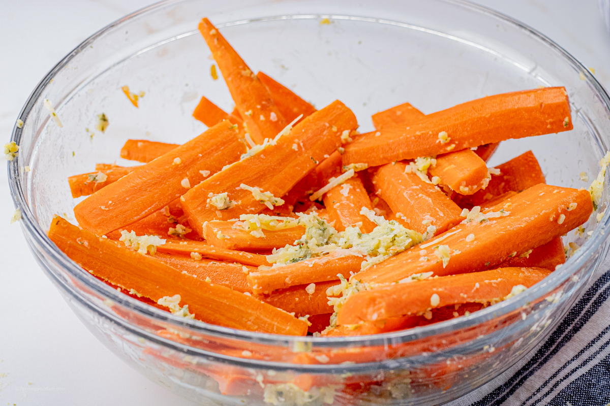 sliced carrots tossed with garlic parmesan butter in a glass mixing bowl