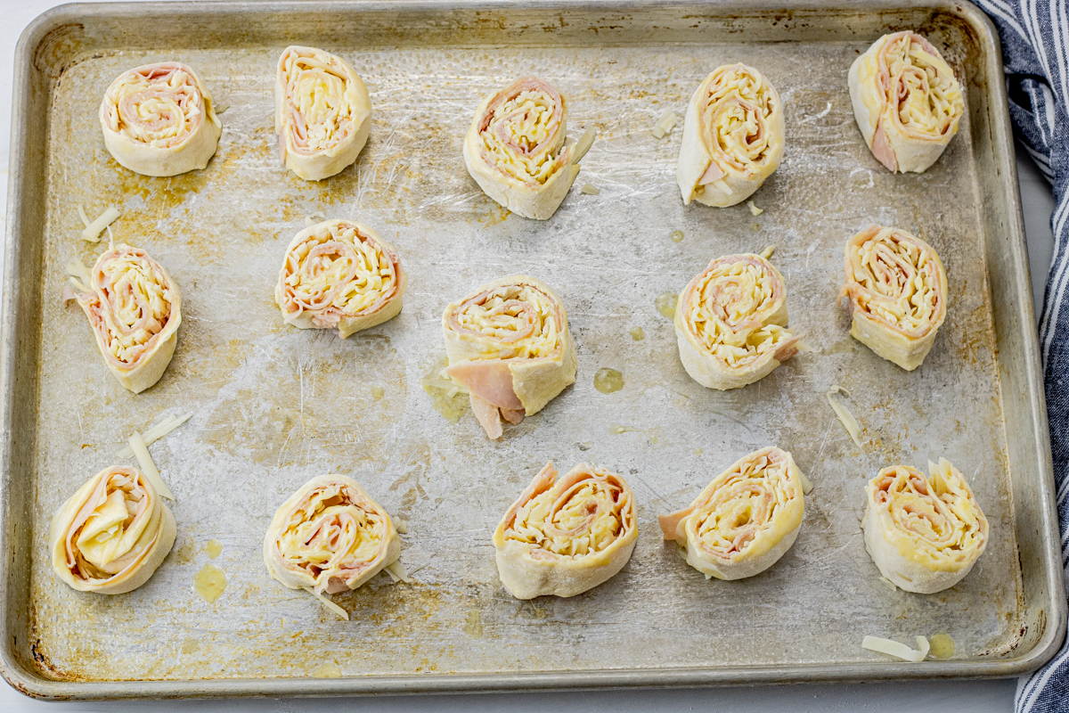 rolled up ham and cheese puff pastry rolls on a baking sheet, uncooked
