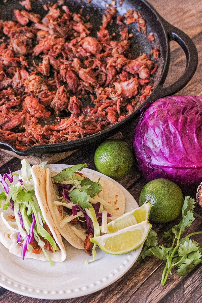 cast iron pan with shredded pork and a plate with two tacos on it