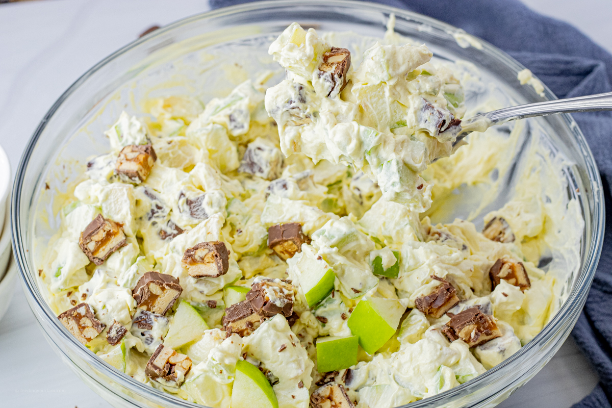 chopped snickers and green apples in a vanilla pudding mixture in a glass mixing bowl