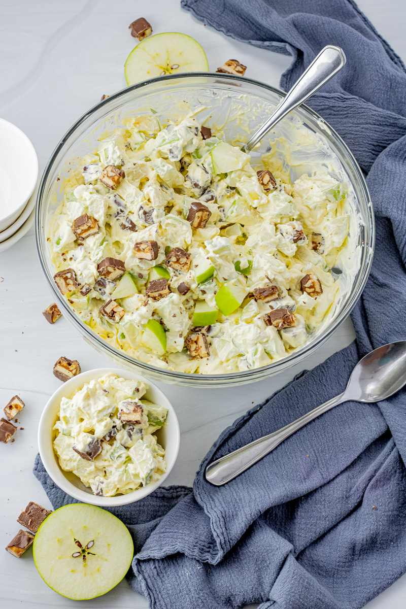 glass mixing bowl filled with a pudding based salad with snickers and green apples