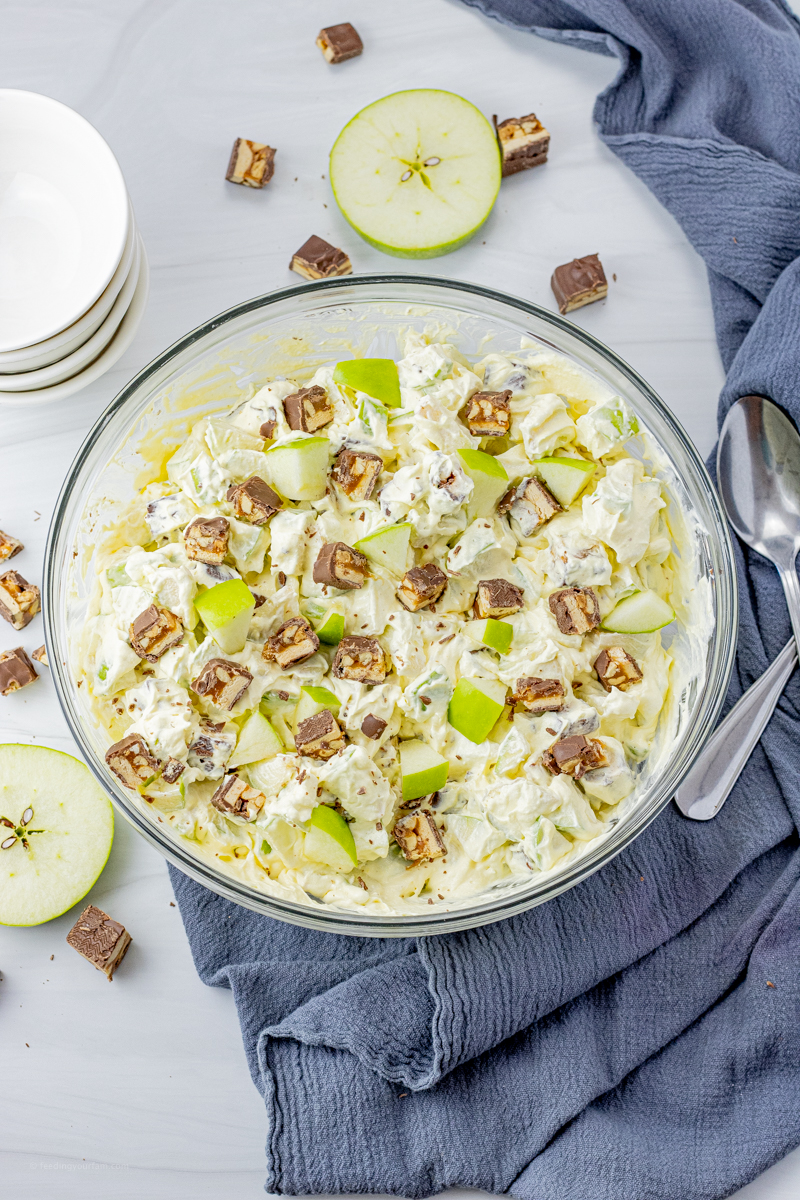 chopped snickers, green apples in a vanilla pudding mixture in a glass mixing bowl