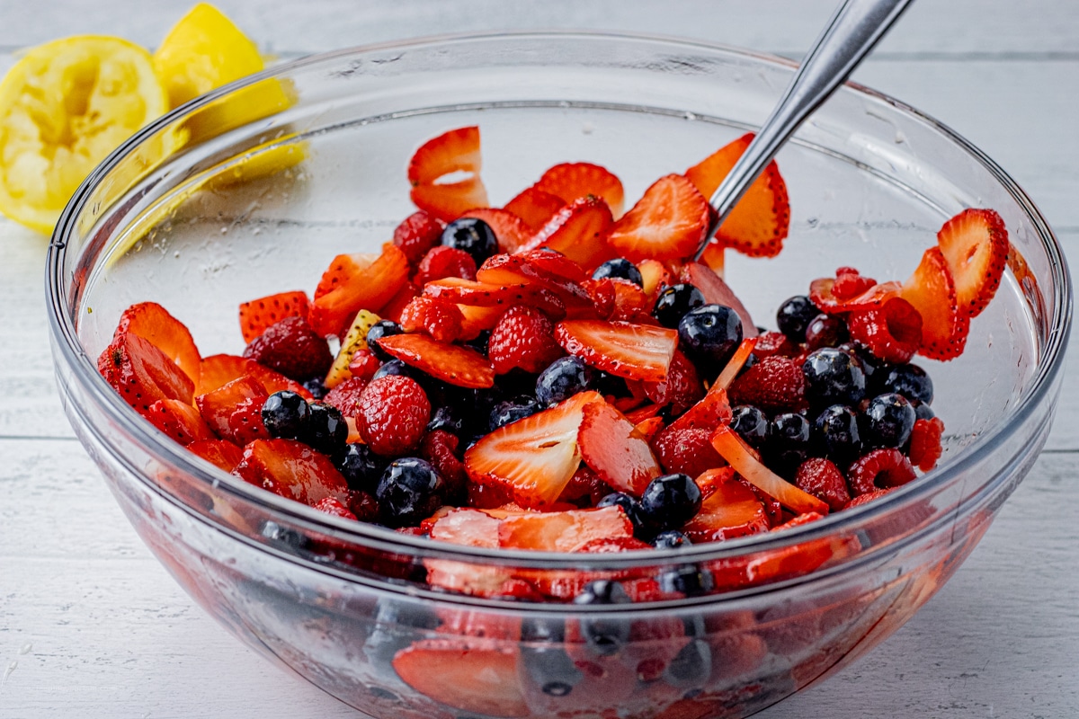 mixed berries in a glass mixing bowl marinating in honey and lemon juice