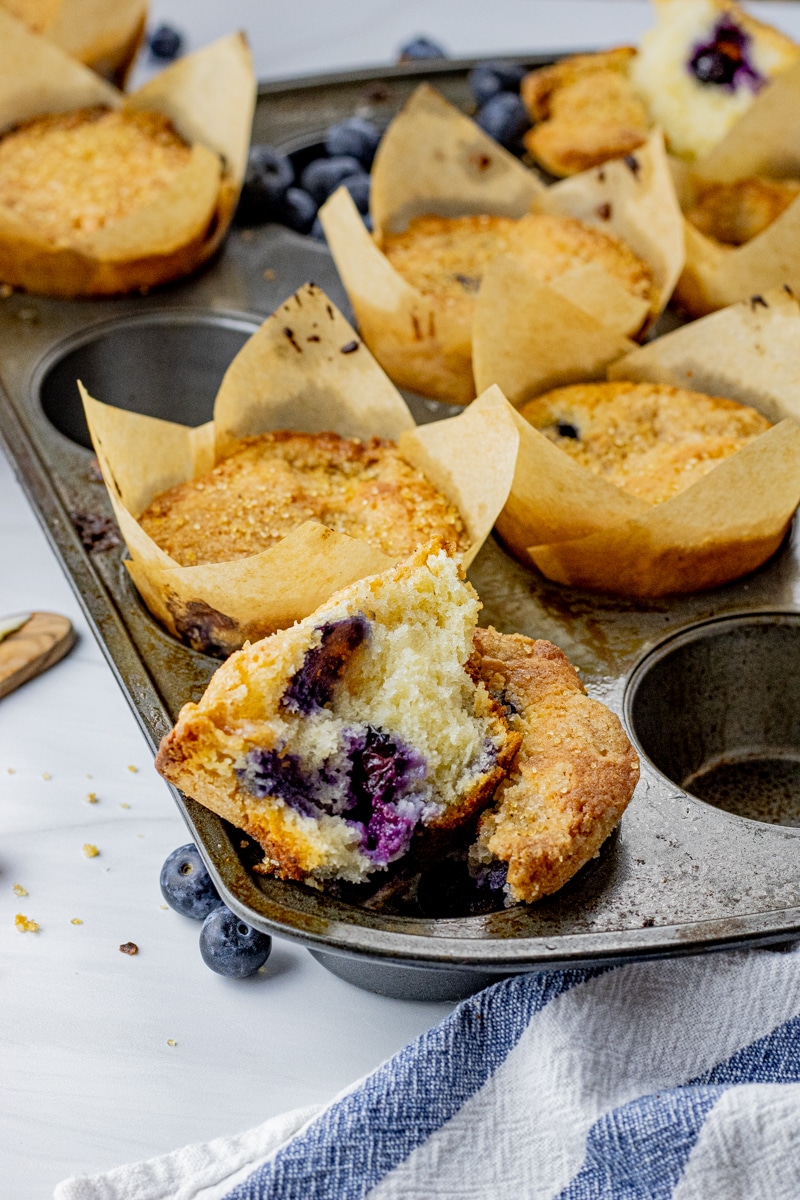 blueberry muffins in a muffin pan with one broken in half