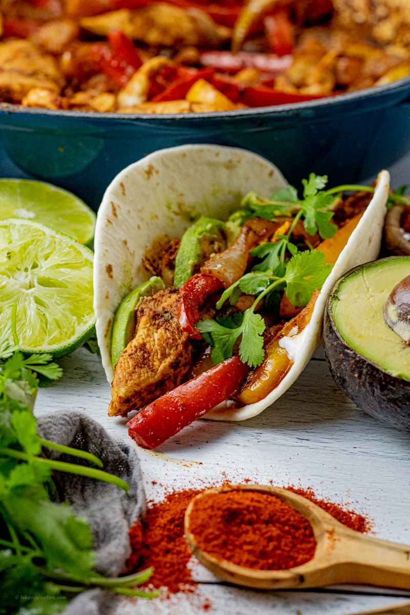 chicken fajita mixture in a flour tortilla with limes and avocado next to it