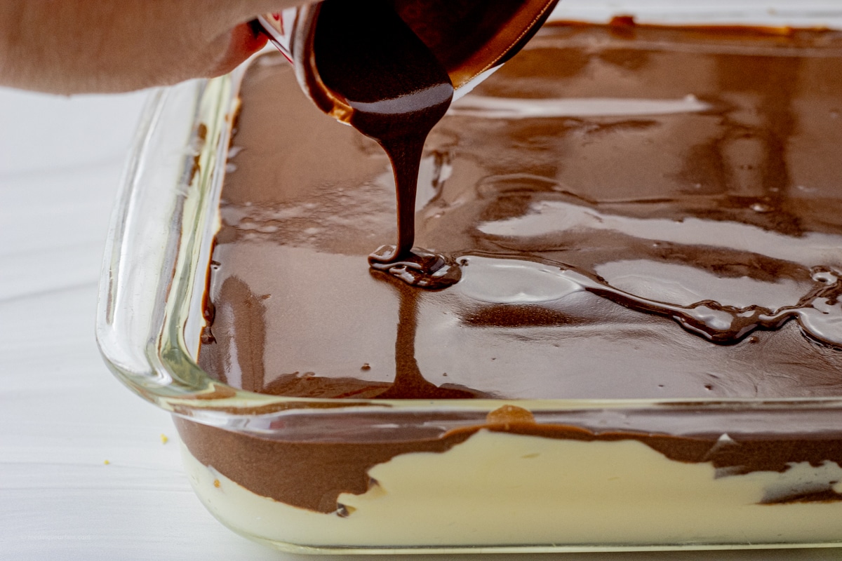 hand pouring chocolate frosting from a frosting container over a cake in a glass pan