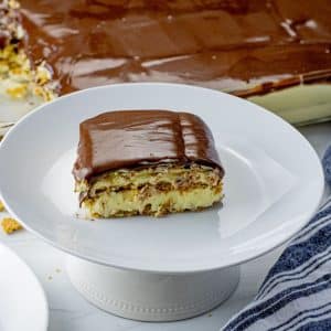 slice of layered eclair cake with graham crackers, vanilla pudding and chocolate frosting on a white plate