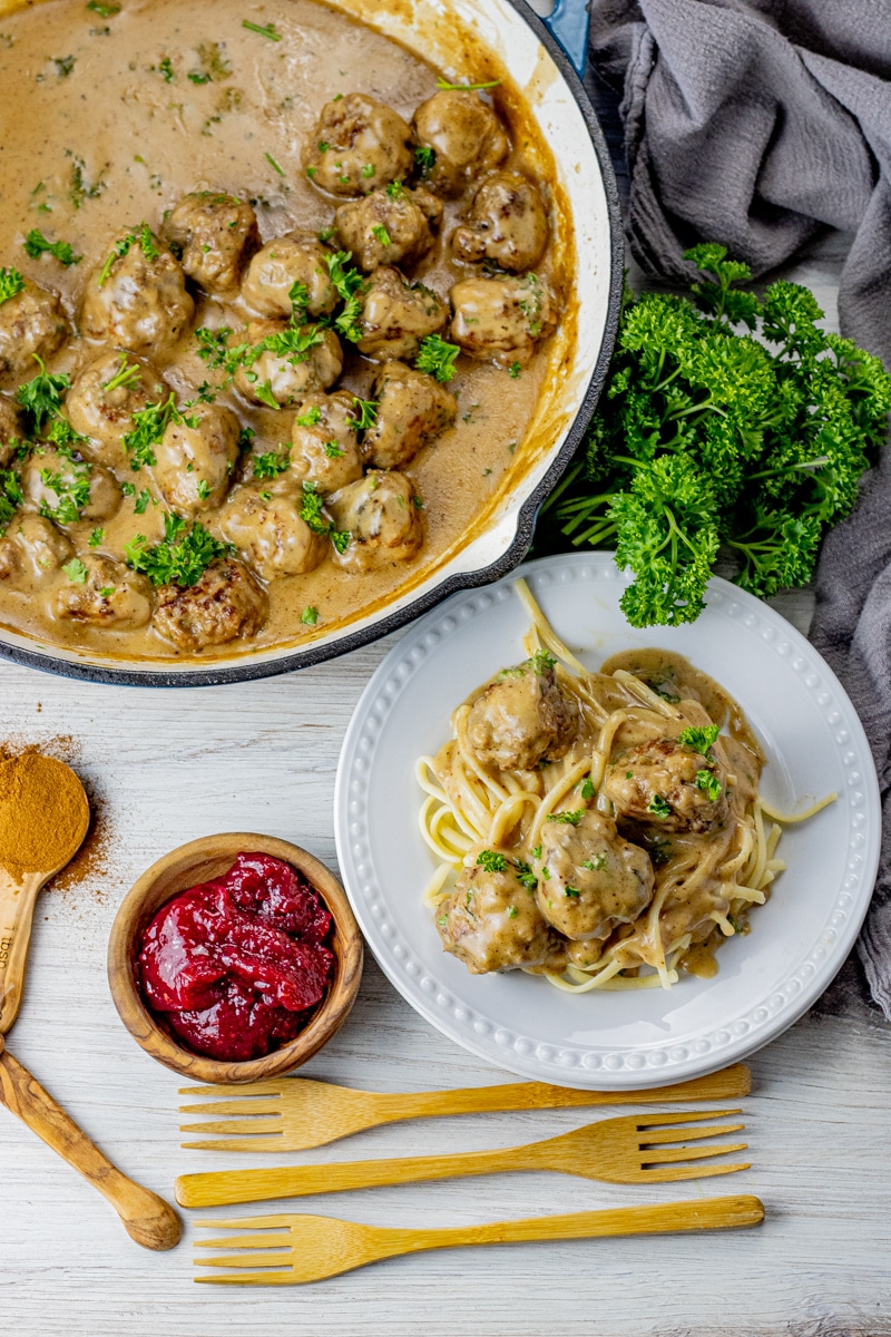 cooked swedish meatballs in a brown gravy sauce, some in a large pan and others on a white plate.