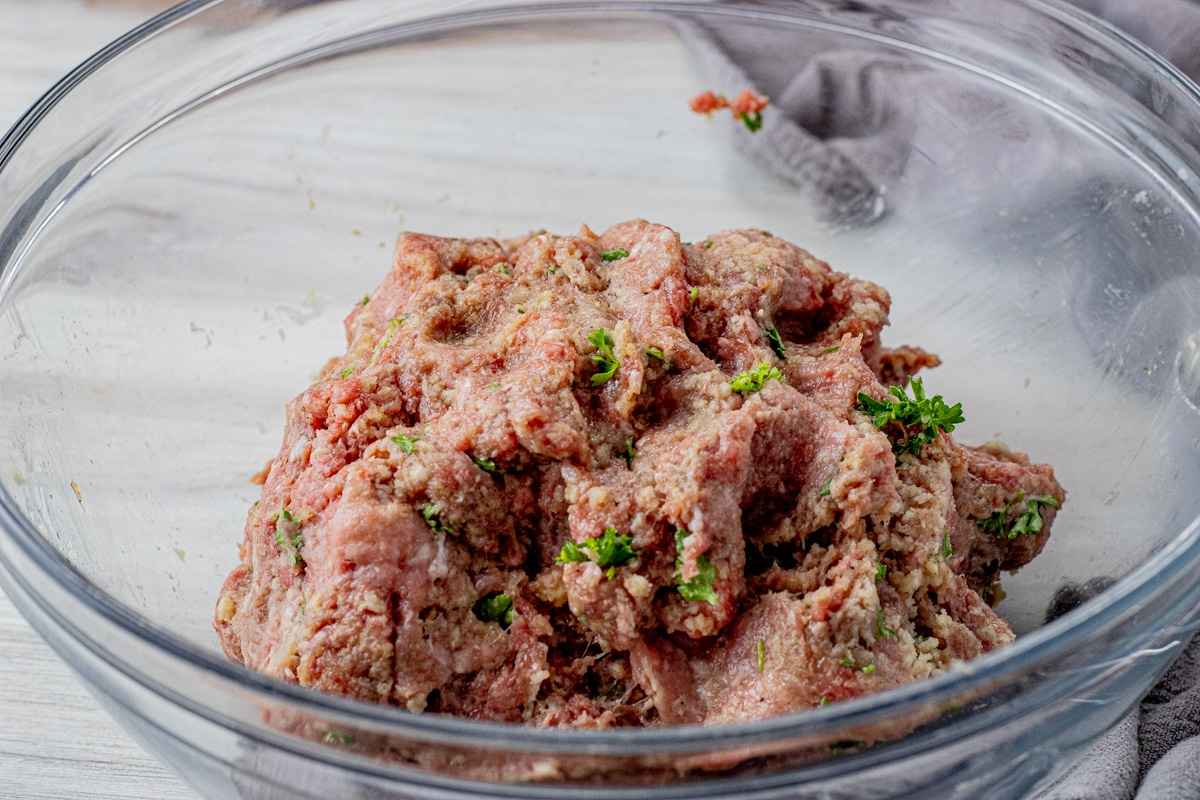 ground beef and pork mixed to make a meatball mixture, combined in a glass mixing bowl
